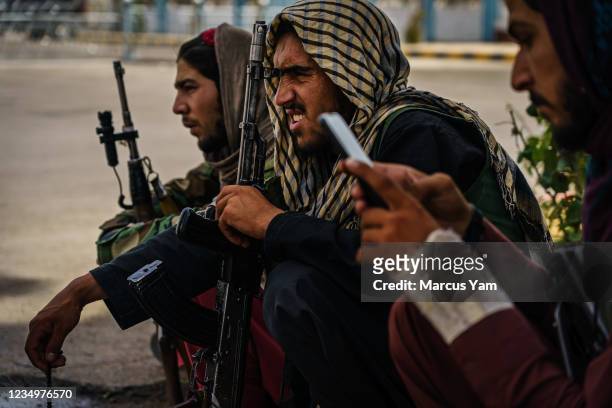 Taliban fighters take shelter from the hot sun as they guard the entrance to the civilian terminal of the Hamid Karzai International Airport, after...