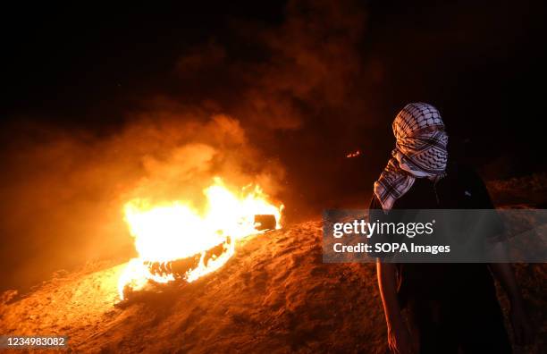 Palestinian seen masked in his background is a burning tire during a protest along the border fence with Israel, east of Al-Buriij refugee camp...