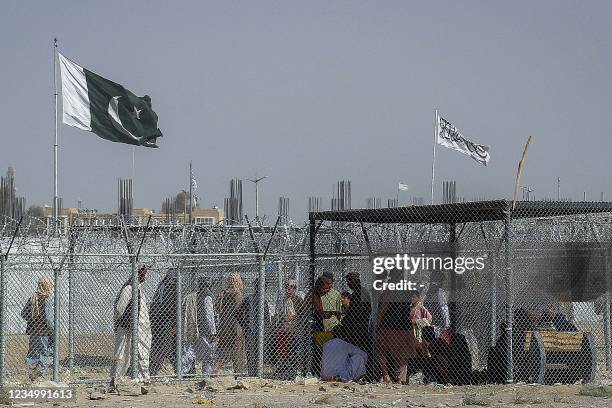 Afghan and Pakistani nationals walk through a security barrier to cross the border as a national flag of Pakistan and a Taliban flag is masted in the...