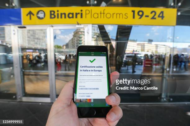 In this photo illustration a hand holding a smartphone with the positive result of the Green Pass verification, in front of the Naples train station....