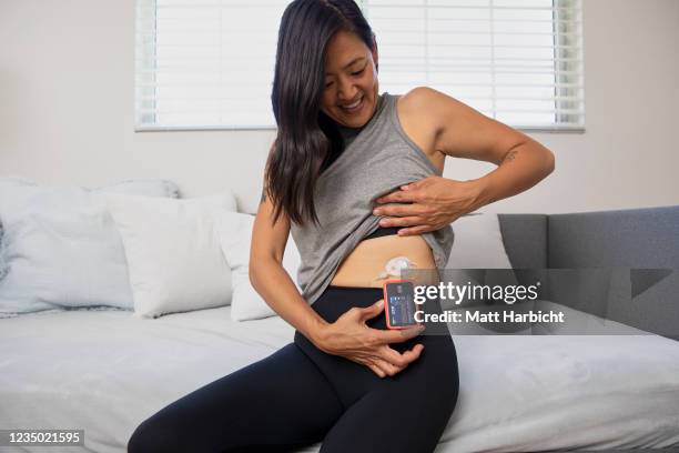 In this photo illustration, a woman in workout gear sits on the edge of a couch and lifts her shirt to reveal an illuminated insulin pump and tubed...