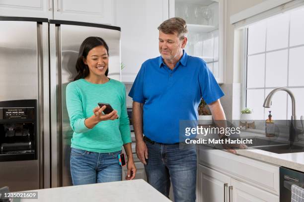 In this photo illustration, two casually-dressed people with type-1 diabetes wearing insulin pumps look at a phone screen in the kitchen.