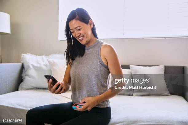 In this photo illustration, a young woman sits on the edge of her bed checking her smartphone while holding her insulin pump.