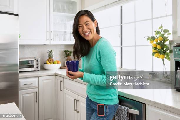 In this photo illustration, a young woman with type-1 diabetes wearing a teal long-sleeved shirt in bright white kitchen holds a blue coffee mug.