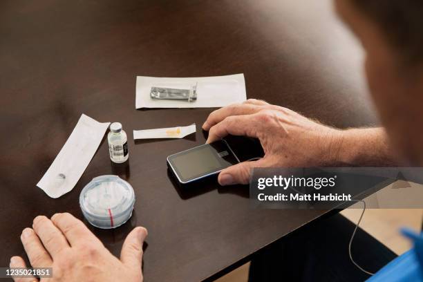 In this photo illustration, a man looks at his supplies for type-1 diabetes management, including tubed insulin pump, insulin vial, syringe, needle,...