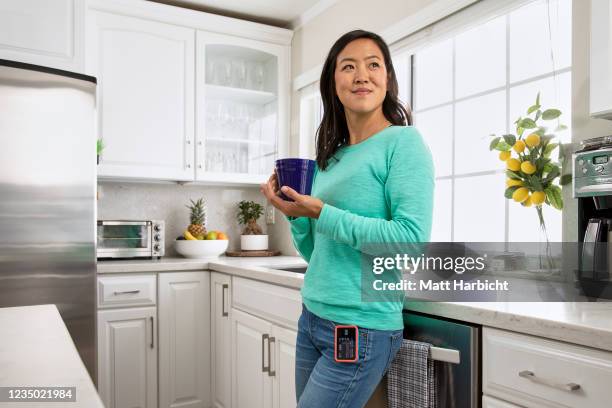 In this photo illustration, a woman in a modern kitchen leans against the counter enjoying her morning coffee in a blue coffee mug while wearing an...