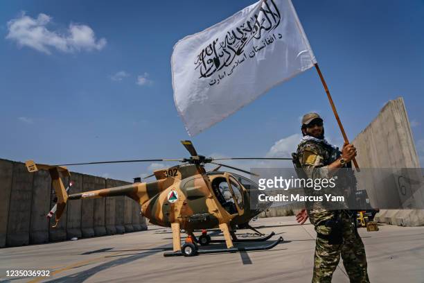 Taliban fighter raises the movementÕs flag as they take a tour of the military assets that were left behind on the military airbase side of the Hamid...
