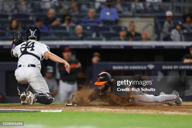 Austin Hays of the Baltimore Orioles scores on a single by Ryan Mountcastle as catcher Gary Sanchez of the New York Yankees reaches for the ball in...