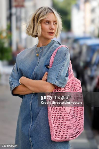 Influencer Lisa Hahnbueck wearing a blue denim jeans mini dress with short sleeves by Prada, a pastel pink crocheted bag by Prada, a gold B.zero1...