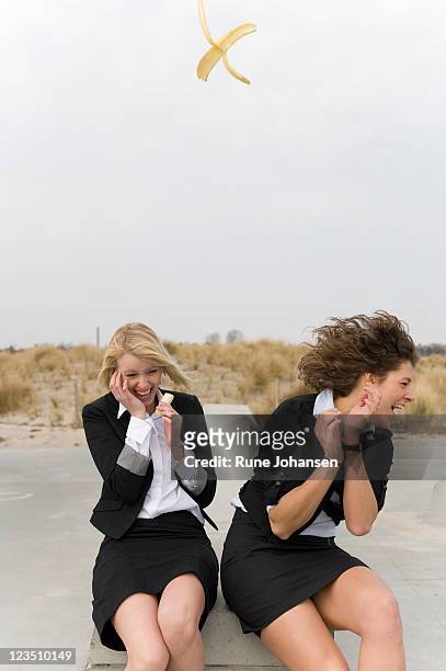 two women eating bananas with one peel tossed in mid-air - wegduiken stockfoto's en -beelden