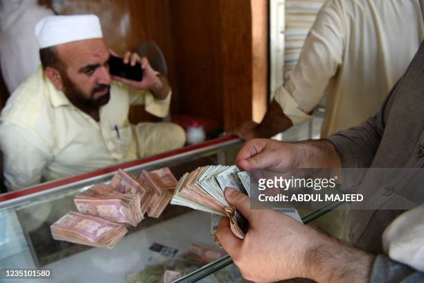 Money changer counts Afghanistan's banknotes afghani in a market in Peshawar on September 7, 2021.