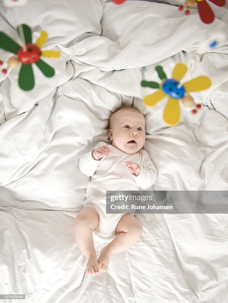 Danish baby girl lying down on bed looking up at a toy mobile