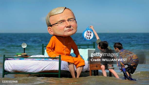 Two boys inspect a man wearing a caricature head of Australian Prime Minister Kevin Rudd in pyjamas while sitting on a bed at St Kilda beach in...