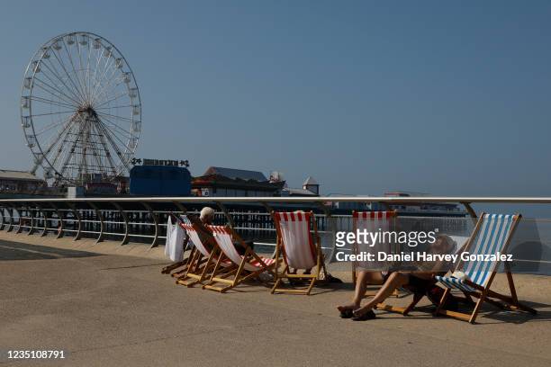 People lounge sunbathing in striped deck chairs, which were banned during the height of the Covid-19 pandemic, with Blackpool's Big Wheel in the...