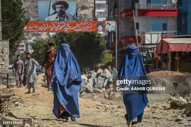 Banner with a picture of late Afghan commander Ahmad Shah Massoud is installed next to residential buildings as burqa-clad Afghan women walk along an...