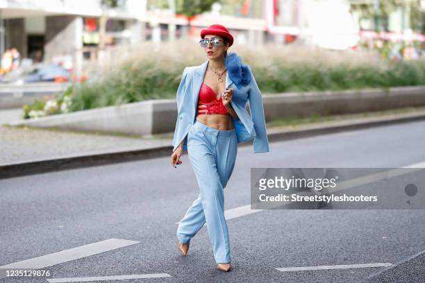 Influencer Salome Chaboki wearing a pastel blue suit with a large flower brooch by Plakinger, a red bralette by Hunkemoeller, a red hat by Giuseppe...