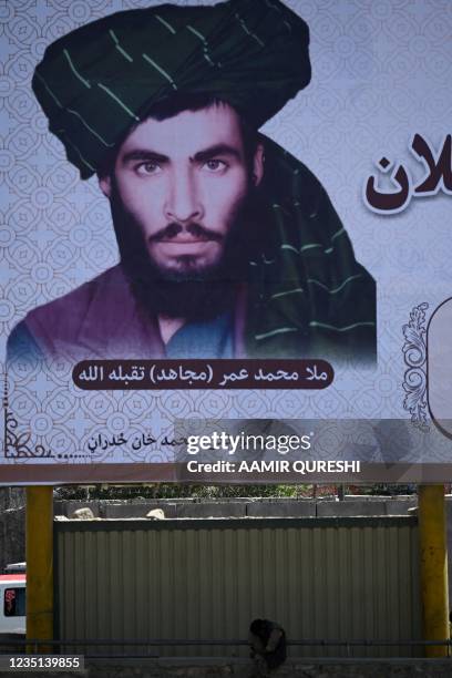 Man sits under a billboard with the image of late Afghan Taliban leader Mullah Omar along a road in Kabul on September 9, 2021.