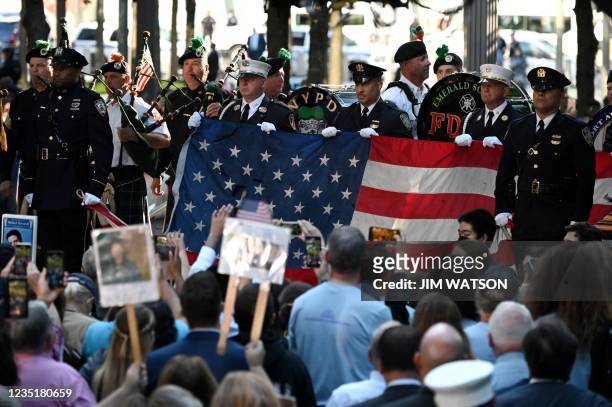 New York police and firefighters hold a US flag as a band plays the US National Anthem at the National 9/11 Memorial during a ceremony commemorating...