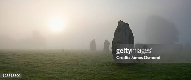 mist surrounds neolithic standing stones at sunrise near avebury in wiltshire. - stone circle stock pictures, royalty-free photos & images
