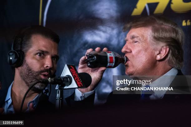 Former US President Donald Trump drinks a soda as he hosts the Holyfield vs Belford boxing match live with commentary, next to his son Donald Trump...