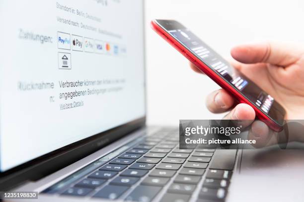September 2021, Baden-Wuerttemberg, Rottweil: A man holds his smartphone for two-factor authentication while a laptop screen displays various payment...