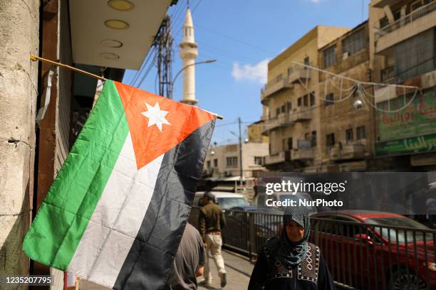 An elderly woman wearing a national headscarf walks past the national flag of Jordan on a shopping street in Amman. Jordan, Sunday, September 12, 2021