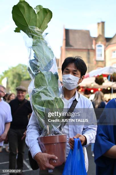 Man wearing a protective face mask carries a plant along the street at Columbia Road flower market in east London on September 12, 2021. The weekly...