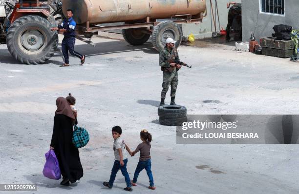 Picture taken during a tour organized by the Syrian Ministry of Information shows people walking past Syrian soldiers at a checkpoint in the district...