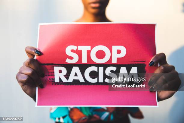 woman holding a red sign agains racism - racism imagens e fotografias de stock