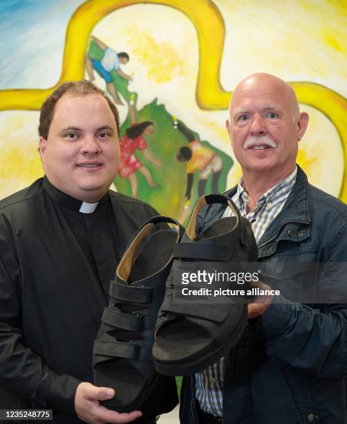 September 2021, North Rhine-Westphalia, Essen: Shoemaker Georg Wessels shows the new sandals for the world's largest feet with Father Alejandro Keri...