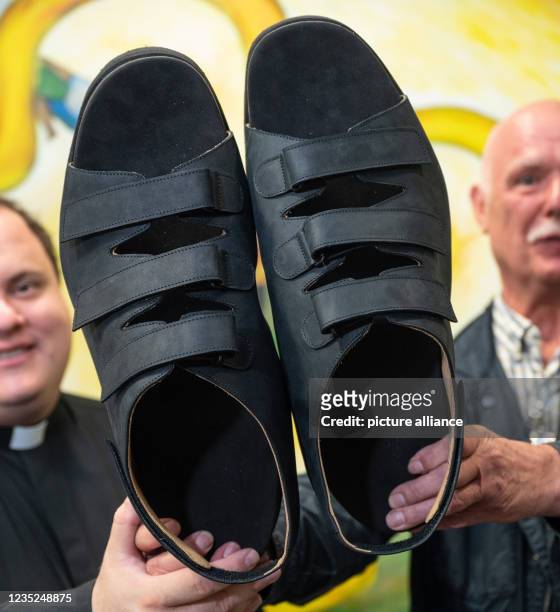 September 2021, North Rhine-Westphalia, Essen: Shoemaker Georg Wessels shows the new sandals for the world's largest feet with Father Alejandro Keri...