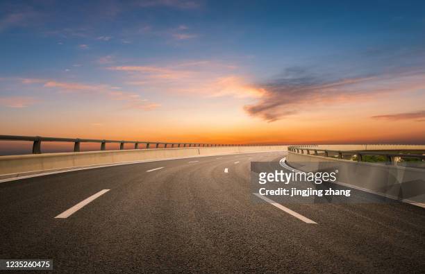 dusk colored clouds in the background, highway overpass curved approach bridge - street sunset stock-fotos und bilder