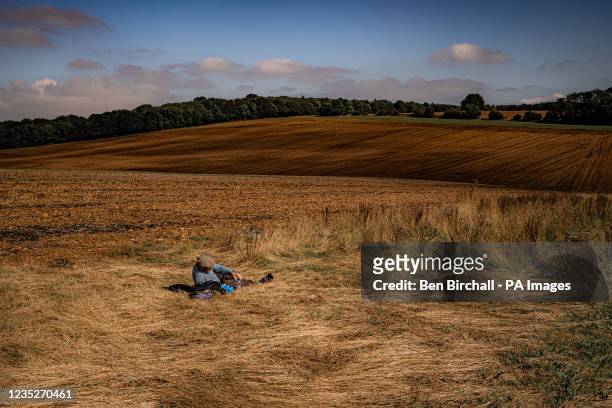 Man takes a rest in a stubble-burned field on a sunny day, where low fluffy clouds cast shadows on the Cotswold landscape near Snowshill. Picture...