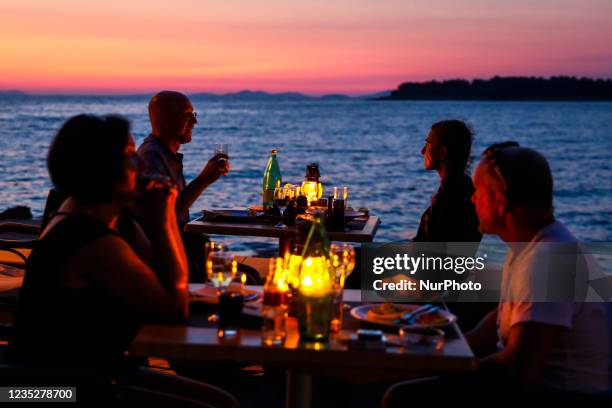 People are sitting at the restaurant by the sea during a sunset in Primosten, Croatia on September 12, 2021.