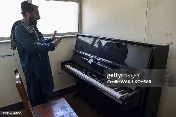 This photo taken on September 14, 2021 shows a member of the Taliban showing a piano at the Afghanistan National Institute of Music in Kabul. - The...