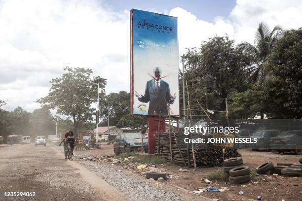 Two women walk past a defaced billboard of former President of Guinea, Alpha Conde, in Conakry on September 16, 2021. - Colonel Mamady Doumbouyas...