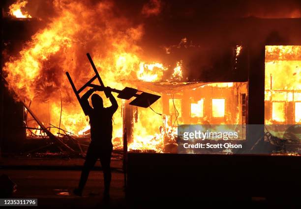 Man holds up a sign near a burning building during protests sparked by the death of George Floyd while in police custody on May 29, 2020 in...