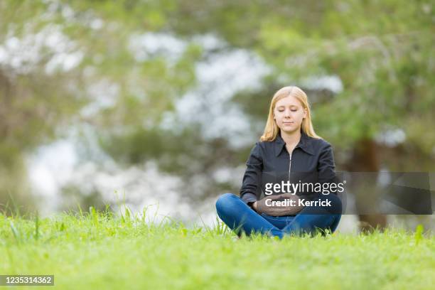 young woman meditating alone on a meadow - yoga - teenager meditating stock pictures, royalty-free photos & images