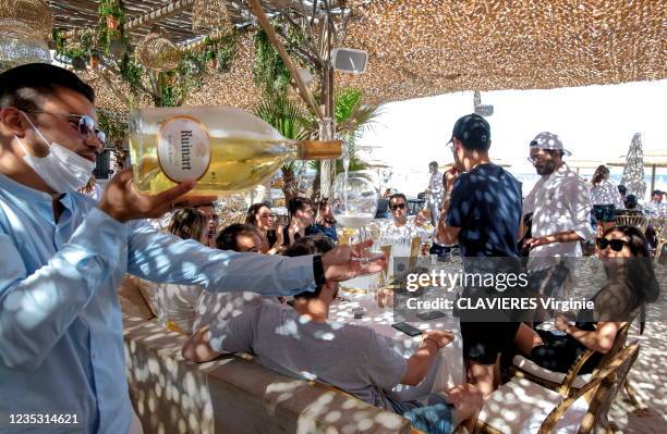 Waiter serves a magnum of Ruinart champagne to customers of the Shellona beach restaurant on July 15, 2021 on Pampelonne beach in Ramatuelle.