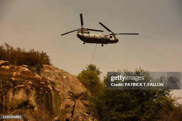 Boeing CH-47 Chinook firefighting helicopter carries water to drop on the fire as smoke rises in the foothills along Generals Highway during a media...