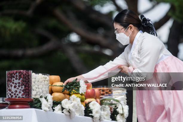 Woman wearing a traditional Hanbok dress places a white flower onto an altar with offerings for families with relatives and ancestors in North Korea,...