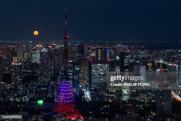 The full moon and Tokyo Tower are seen from the observation deck of Roppongi Hills in Tokyo on September 21, 2021.