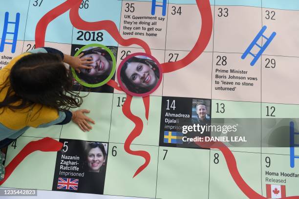 Gabriella Ratcliffe, daughter of jailed British Iranian aid worker Nazanin Zaghari-Ratcliffe moves portraits of her mother on a giant snakes and...