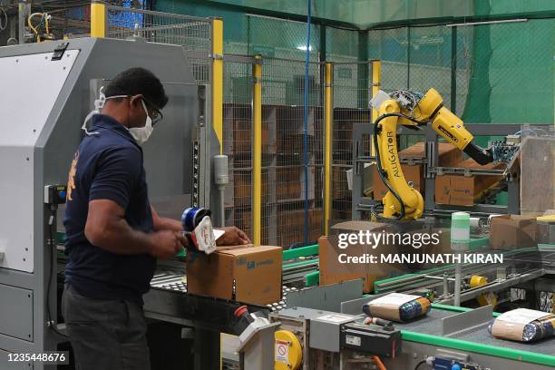 Worker places assorted products into cardboard boxes prepared by robotic arms at the Flipkart fulfilment centre in Bangalore on September 23 ahead of...