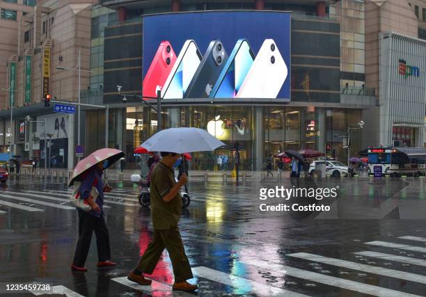 People walk past an advertisement for the new iPhone13 series displayed on a large screen at the apple store in wangfujing on September 24, 2021 in...