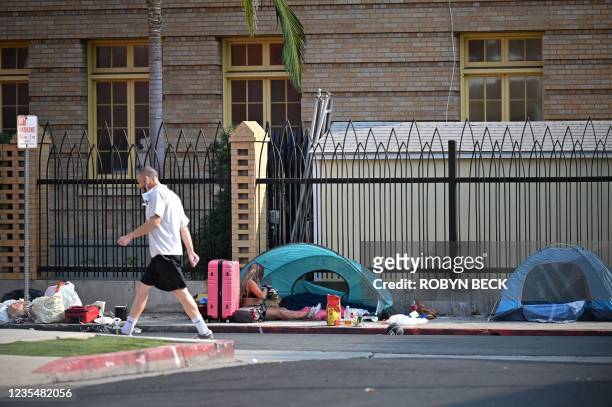 Man walks past a woman and man seen next to a tent on a sidewalk of Hollywood, Los Angeles, California, September 24, 2021. - Los Angeles has seen a...