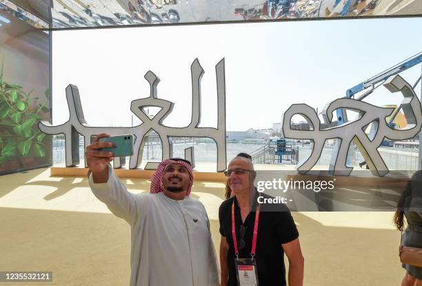 Visitor takes a selfie with Israeli pavilion official Josh Bendit in front of a sign reading "to the future" in words written in ancient characters...