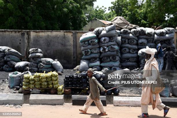 Beggar is being led by an helper as they walk past piles of 15kg bags of charcoal displaced for sale along the road, which many people use for...