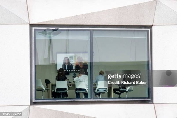 Seen through the window of a corporate office workplace, staff participate in a Zoom meeting in the City of London, the capital's financial district,...