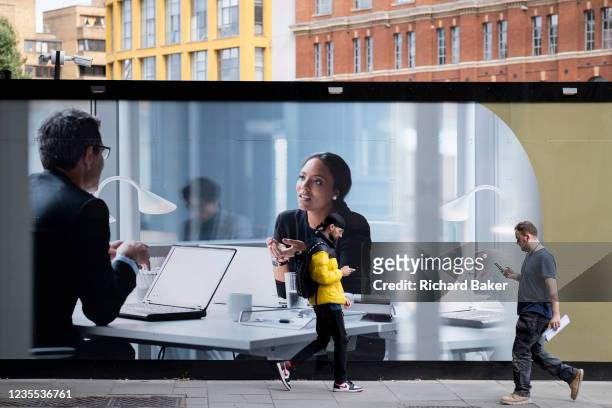 As two strangers walk towards each other while distracted by their phones, work colleagues appear on a corporate billboard making eye contact, in a...